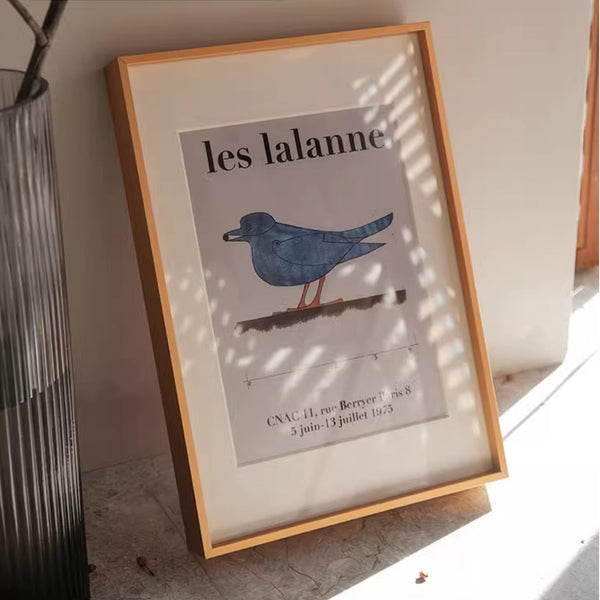 Black aluminum picture frame with artwork showing a bluebird illustration and text on a light surface.