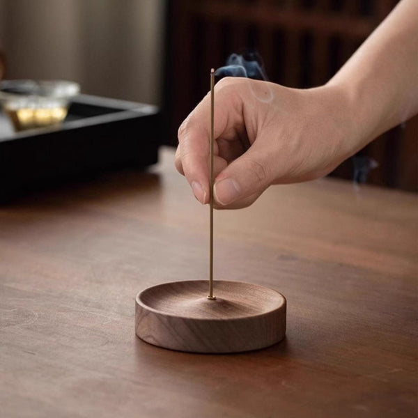 Hand lighting an incense stick on a black walnut incense stand with a blurred background