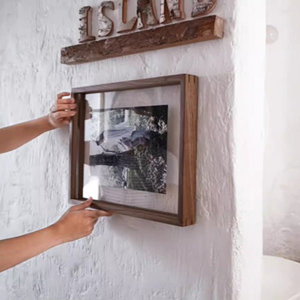 A person hanging a black walnut wooden picture frame on a white wall with 'ISLAND' decor above.