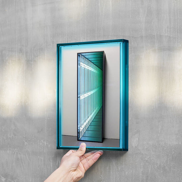 Hand holding a blue rectangular acrylic picture frame against a gray wall.