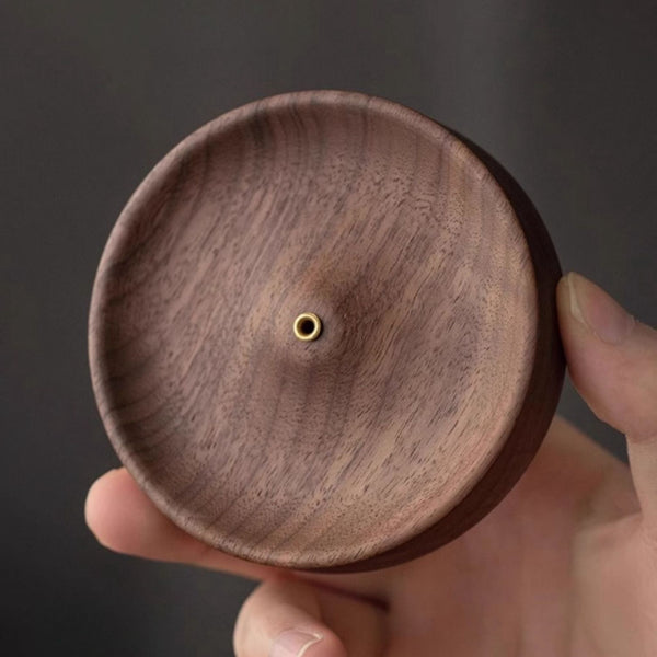 Hand holding a black walnut round incense holder with a central hole against a dark background