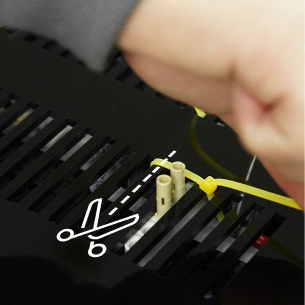 LEGO Technic set wall display installation instruction. Close-up of a hand holding a yellow wire near electronic components with a cut-out scissors icon.