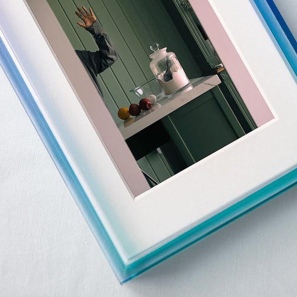 Ombre acrylic picture frame focused corner shot, reflecting a room with decorative items on a shelf.