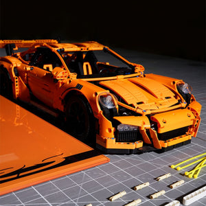 Orange toy car made of interlocking bricks on a dark surface with scattered DIY toolkit pieces.
