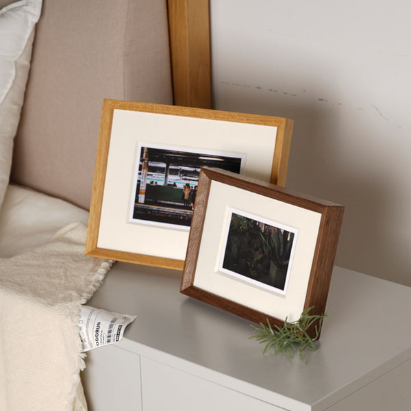 Two wooden picture frames with photos on a surface. Teak and black walnut.