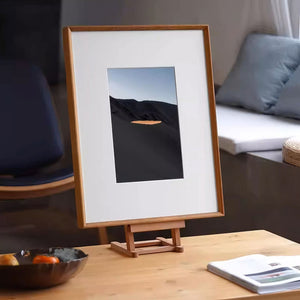 Teak wood-framed photograph of a desert landscape on a wooden stand in a home setting.