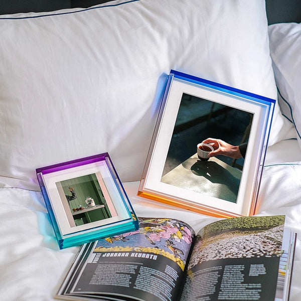 Two ombre acrylic picture frames on a bed next to an open book