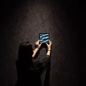 Person holding a small frame with 3D carved blue waves with a dark background