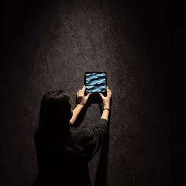 Person holding a small frame with 3D carved blue waves with a dark background