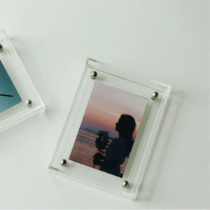 Clear acrylic photo frame with a silhouette of a couple at sunset on a white surface.