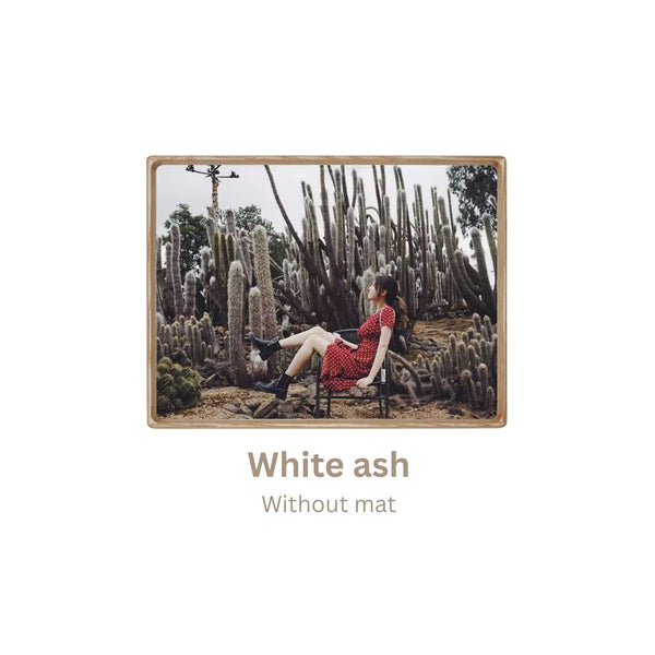 White ash wood-framed photograph of a person in a red dress sitting among cacti with 'White ash, without mat' frame text. 