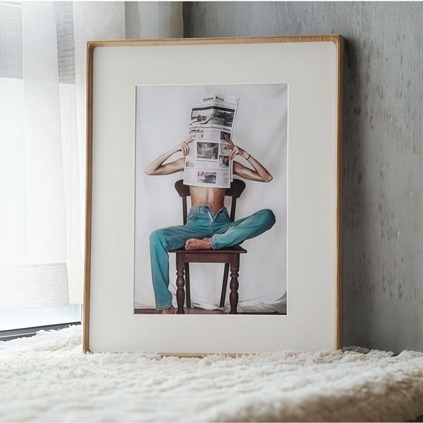 White ash wood framed artwork of a person sitting on a chair reading a newspaper, leaning against a textured wall.