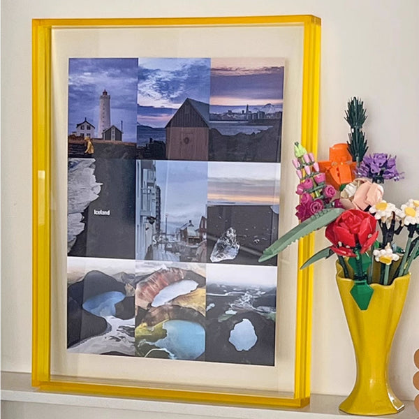 Picture framed collage of landscape photos with a yellow acrylic frame and vase of flowers on a shelf.