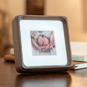 Wooden mini black walnut photo frame displaying a picture on a wooden surface. 4in x 4in. Polaroid fitting.