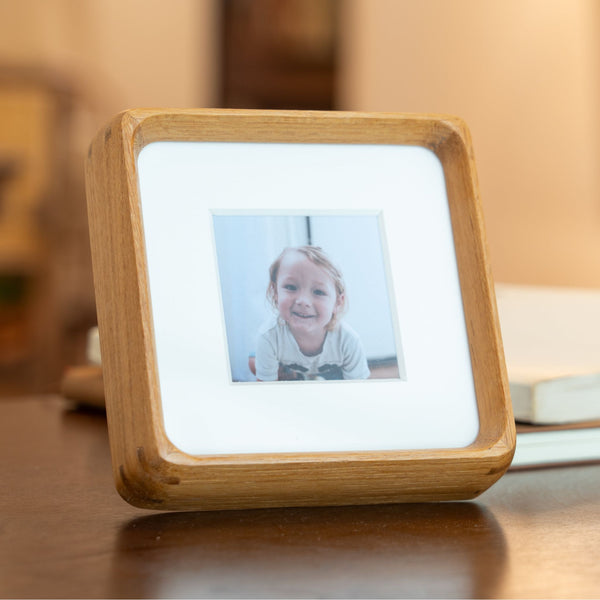 Wooden mini teak photo frame displaying a picture on a wooden surface. 4in x 4in. Polaroid fitting.