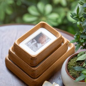Stack of wooden teak mini photo frames with a blurred green plant background. 