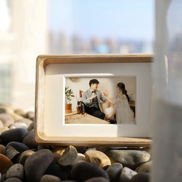 white ash wooden photo frame with a picture of a couple on pebbles by a window