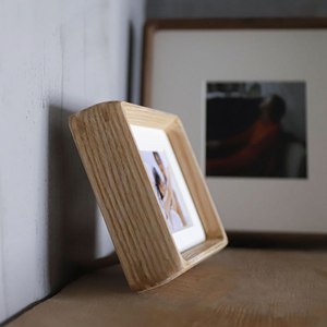 white ash wood photo frame with a picture of a person on a surface, with another framed picture in the background.